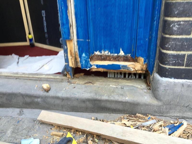Rotten timber at the foot of a wooden shop front door before repair